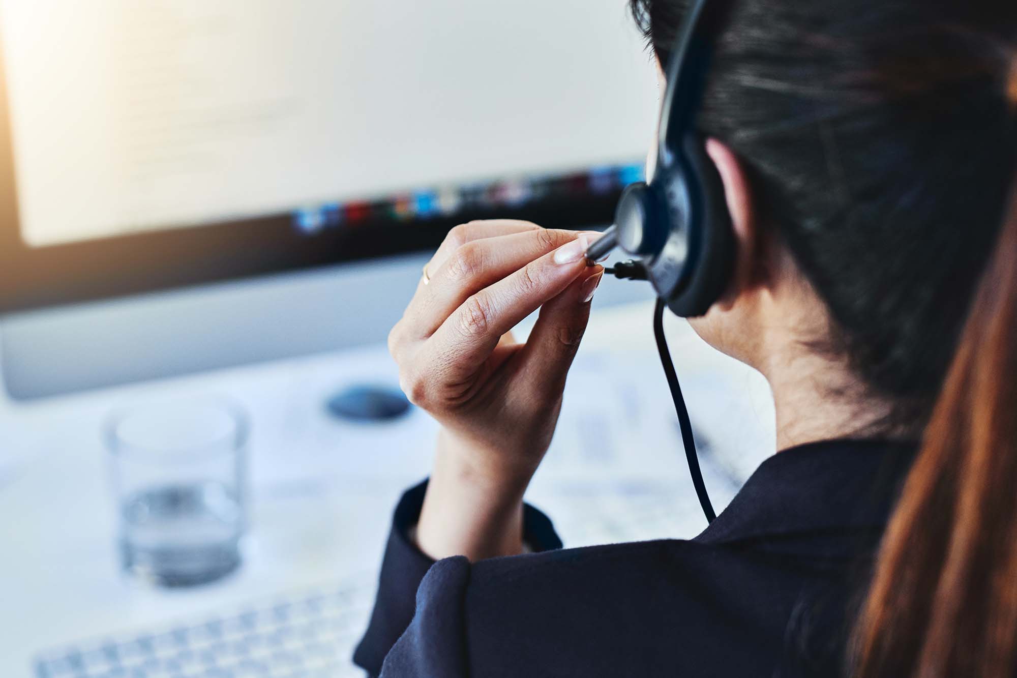 Close-up of a woman wearing a headset and speaking while working at a computer.